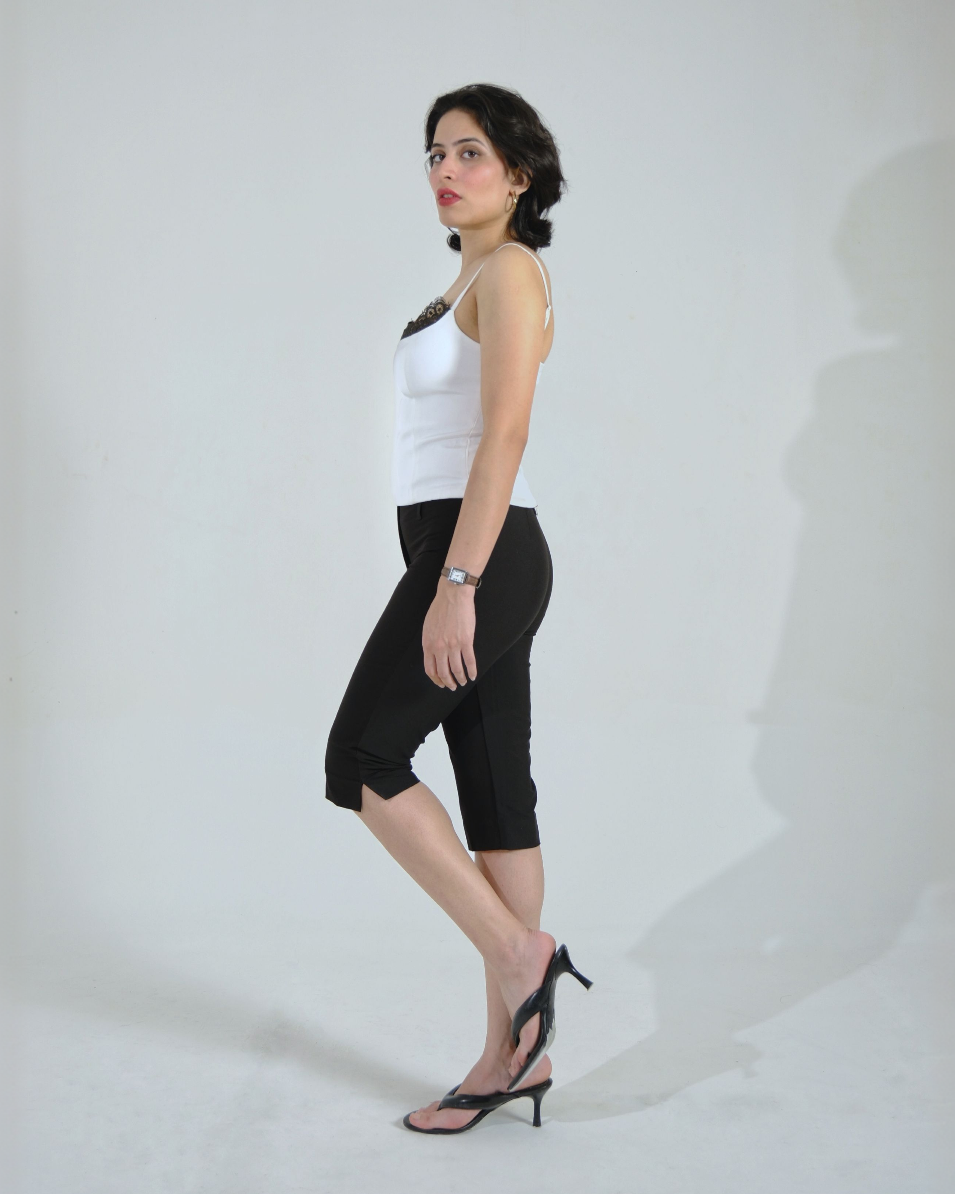 Woman wearing black capri pants with a white top, side view, standing