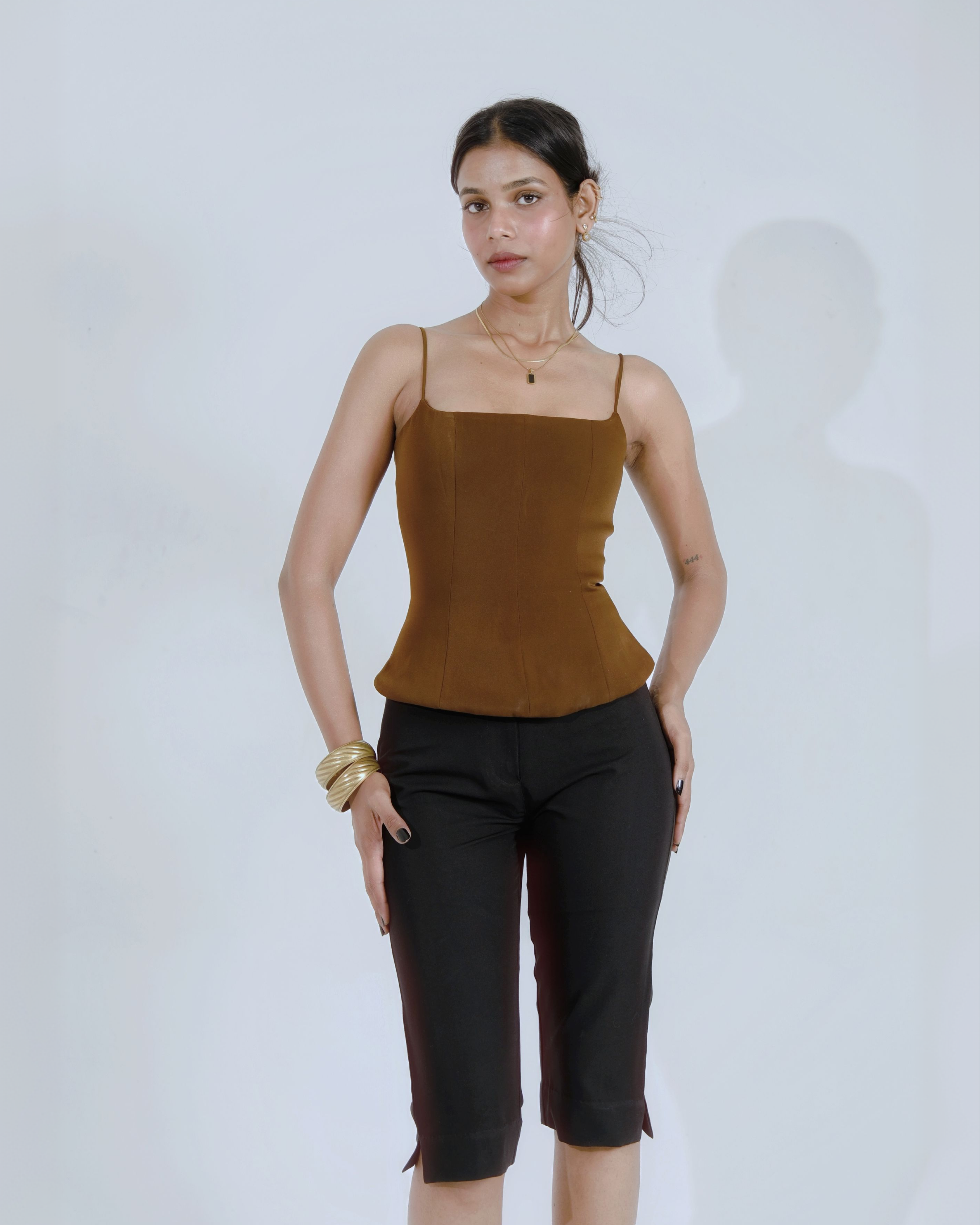 Woman wearing a brown corset-style top with thin straps and cropped black pants, front view