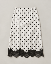 A white midi skirt with black polka dots and a black lace hem, displayed flat against a neutral light gray background.