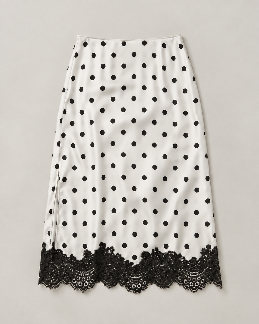 A white midi skirt with black polka dots and a black lace hem, displayed flat against a neutral light gray background.